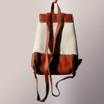Back view of artisanal felt leather backpack held by hand, showing adjustable leather straps and quality hardware