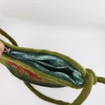 Close-up of needle-felted red poppies and stems on vibrant green wool felt texture of Turkmen handmade purse