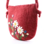Close-up of needle-felted white daisies, purple and blue flowers on rich red wool felt texture of Turkmen handmade purse