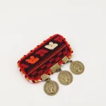 Close-up of handmade Turkmen embroidered brooch with traditional silk needlework and three bronze pendants on black fabric
