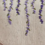 Close-up of handmade Merino wool felt backpack featuring hand-embroidered lavender flowers and natural leather base